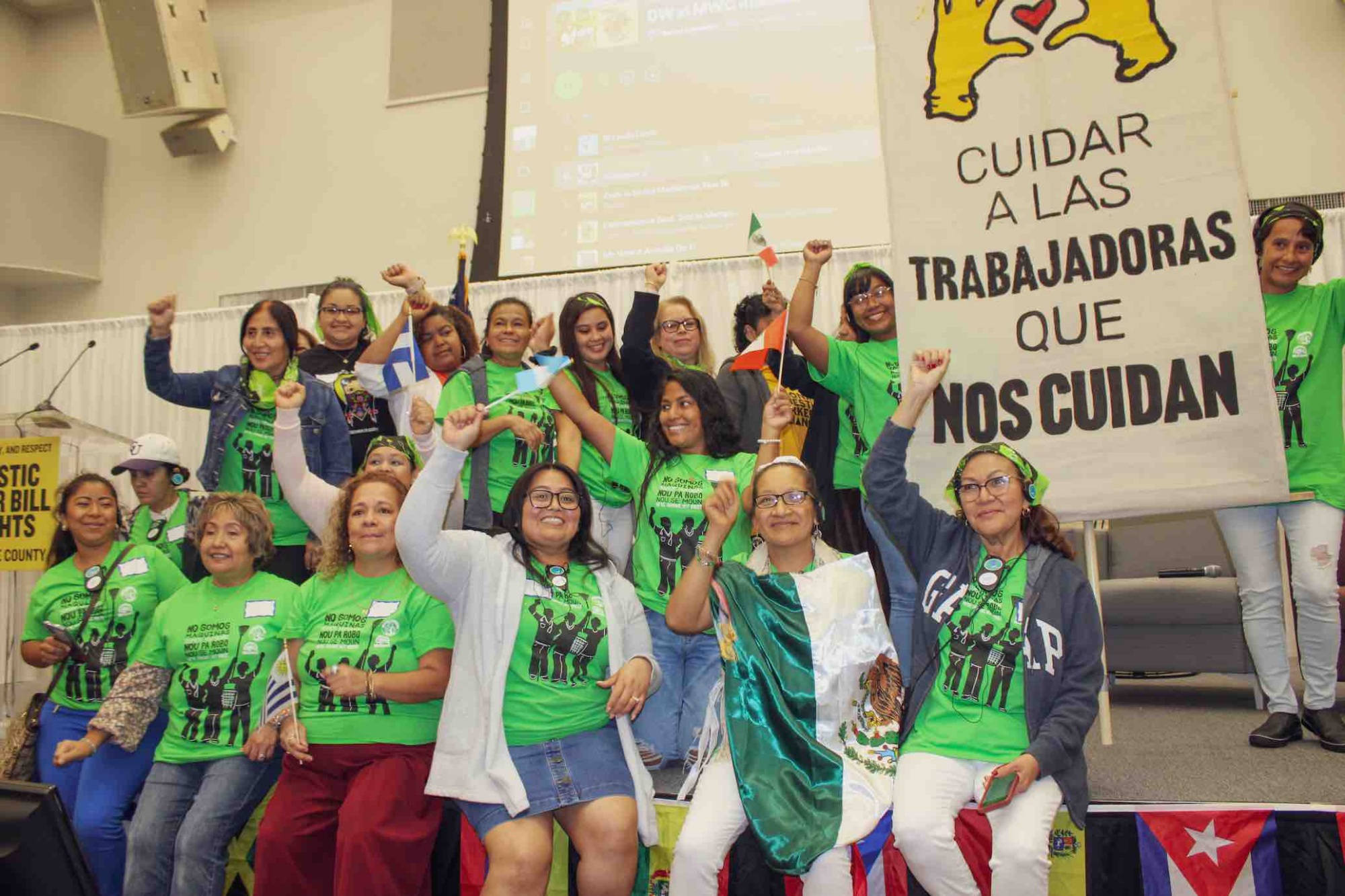 group of care workers from miami workers center wearing matching green shirts, some holding up fists, holding a sign in Spanish